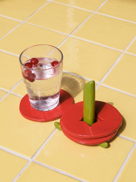 Ceramic tomato coasters on a stalk-shaped stand, with a glass of water on one coaster