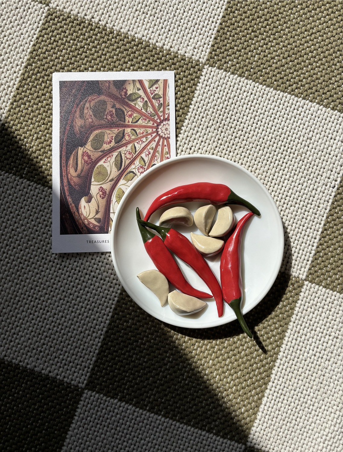 Ceramic chili peppers and garlic cloves on a plate beside a botanical postcard